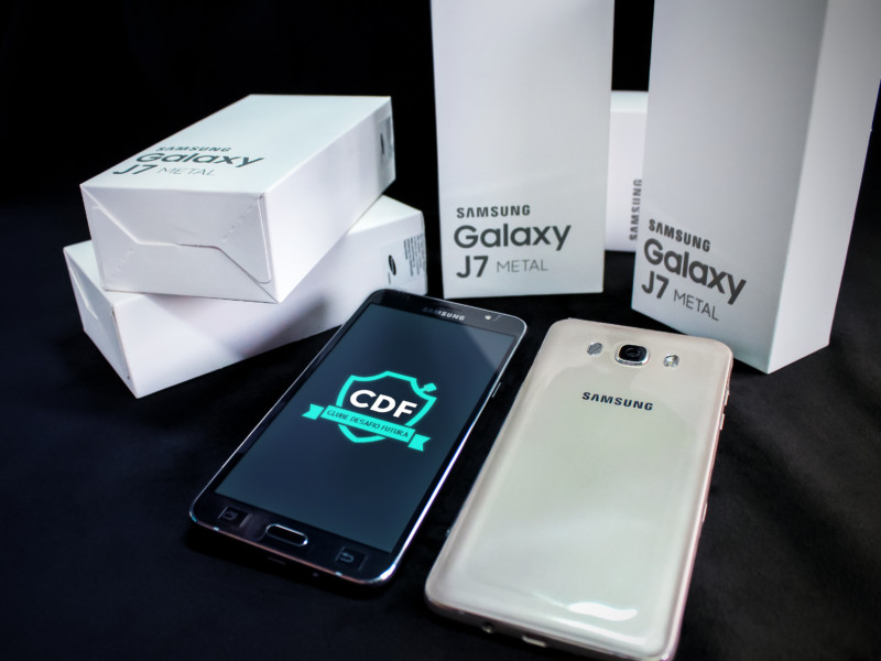 Imagem de cinco embalagens de celular (cinco caixinhas brancas) e dois celulares à frente, um mostrando a tela com o app CDF e o outro com a parte de trás do cel à mostra