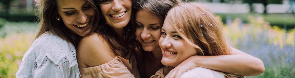 Quatro mulheres amigas estão sorridentes e se abraçando bem felizes