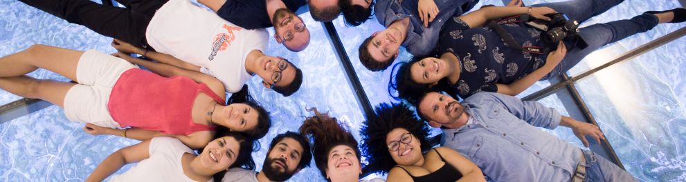 Vários jovens deitados no chão e formando um círculo, um do lado do outro.