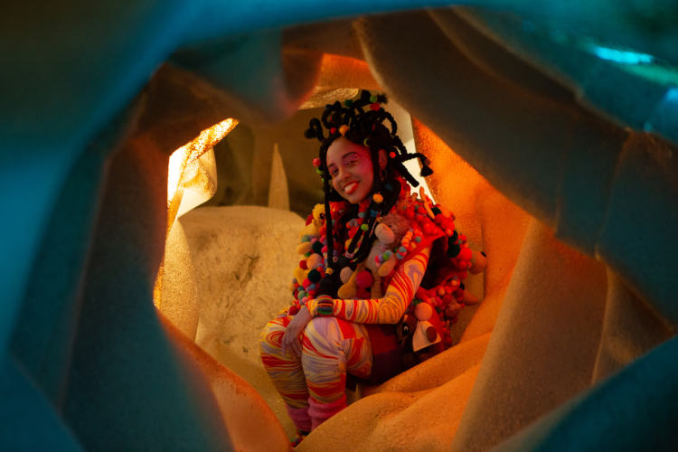 Uma menina negra sentada no que parece ser o interior de uma caverna 